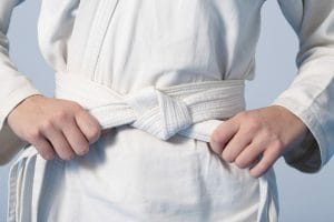 Hands tightening white belt on a teenage dressed in kimono for martial arts, adhd child.